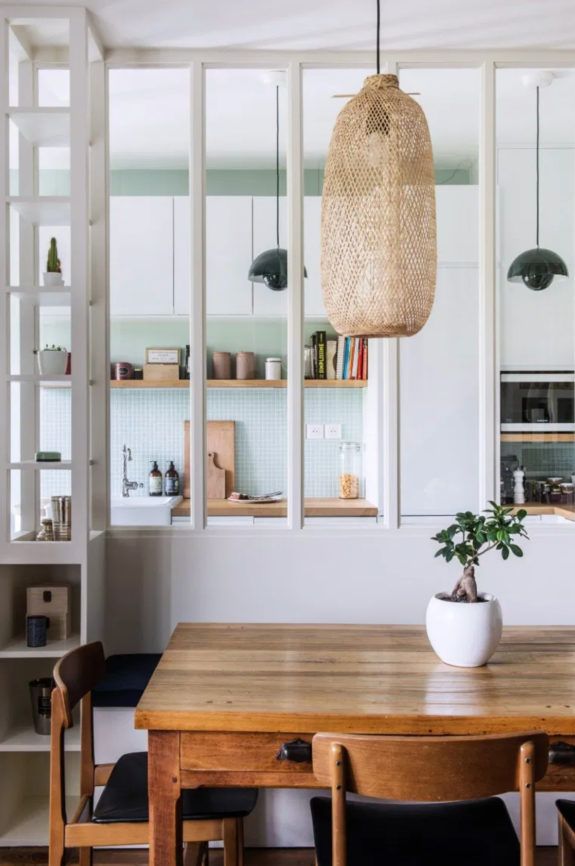 Dining area with wooden table and chairs, wicker pendant light, and bookshelf in the background.