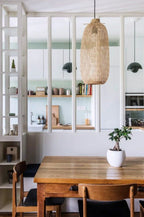 Dining area with wooden table and chairs, wicker pendant light, and bookshelf in the background.